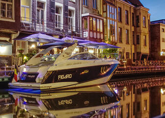Nightly view of houses and restaurants along the water, with yacht Figaro in the foreground.