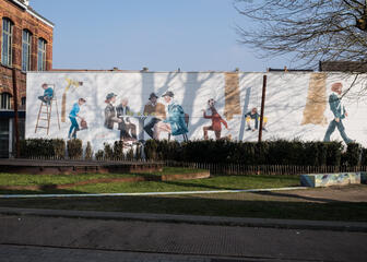 Pierkespark Gent met beschilderde muur op de achtergrond: tekeningen van spelende kinderen, wandelende buren en buurtbewoners rond de tafel met een drankje.