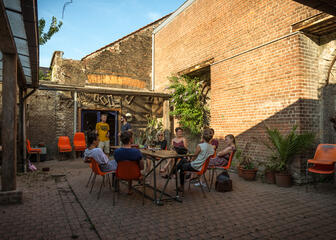 Binnenkoer van Hostel treck in Gent: grote tafel met oranje stoelen waar mensen iets aan het drinken zijn. 