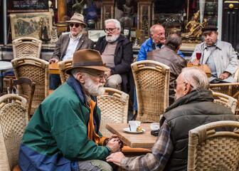 Terras voor Café Bistro en Antiek Montparnasse met oudere mannen aan tafeltjes met rieten stoelen die koffie en bier drinken.