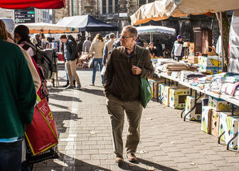 Man bekijkt de brocantemarkt bij Sint-Jacobs met op de achtergrond kraam met linnengoed.