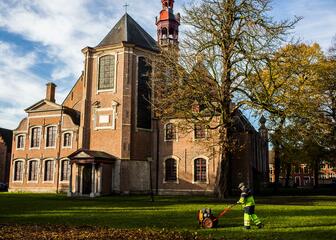 Sint-Elisabethkerk in het Oud Begijnhof met grasplein en tuinman met grasmaaier op de voorgrond.