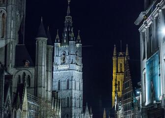 Nachtelijk zicht op de verlichte torens van de Sint-Niklaaskerk, van het Belfort en van de Sint-Baafskathedraal