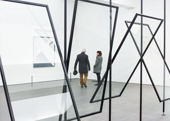 Galerij S.M.A.K. Gent met kunstliefhebbers en op de voorgrond een installatie met kantelende ramen.