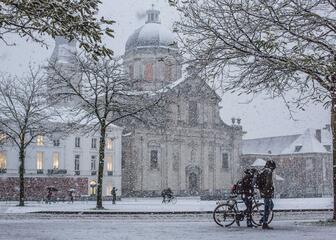 Sint-Pietersplein in een sneeuwbui met de kerk op de achtergrond, twee mensen met de fiets aan de hand vooraan.