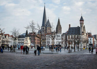 Vrijdagmarkt; groot open plein met boompjes; standbeeld van Jacob van Artevelde: veel torentjes in de verte; veel wandelaars.