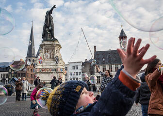 Vrijdagmarkt; iemand maakt grote zeepbellen; kinderen spelen ermee; standbeeld Jacob van Artevelde.