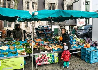 Een mama en haar peuter kopen bio-groenten op de Groentenmarkt