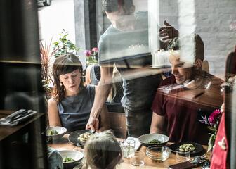 Jong gezin tafelend, kelner door venster gezien.