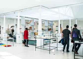 Mensen bezoeken het Design Museum Gent. Witte galerij met kleurrijke objecten.