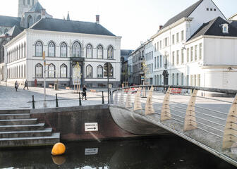 Open pleintje met groot wit Bisschopshuis, op de voorgrond brug en rivier.
