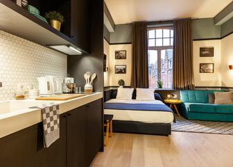 een kamer met een tweepersoonsbed, een blauwe zetel, een zwarte keuken