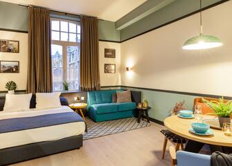 een kamer met tweepersoonsbed, blauwe zetel, enkele foto's aan de muur, een gedekte tafel met stoelen
