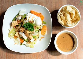 een wit bord met verschillende groenten, vlees en ei, een potje met saus en een potje met een soort chips  