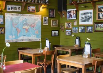 Vierkante houten tafels voor 2, wereldkaarten aan de muur.