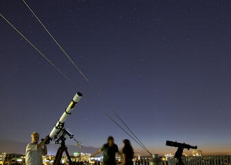 Drie mensen staan op het dak van de Volkssterrenwacht, 's nachts met klare sterrenhemel.