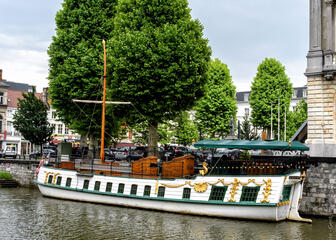 een witte boot met groene en gouden accenten, bomen op de achtergrond