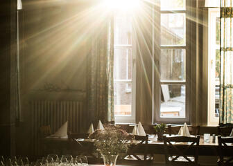 felle zon die door het raam schijnt, lange gedekte tafel met stoelen, tafel met glazen die klaarstaan