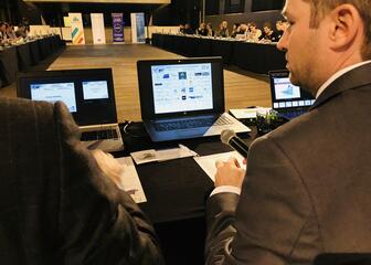 Conferentie: mensen zitten aan lange tafels in U-vorm en kijken naar presentatie