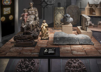 verschillende beelden op een bakstenen tafel, een infobord met kraagsteen uit de bijlokeabdij