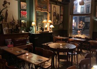 binnenkant café romain met houten tafels en stoelen, de muren hangen vol met oude foto's, een spiegel