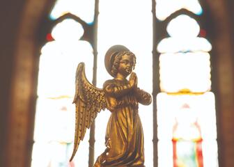 een beeldje van een biddende engel voor een felverlicht glas in-loodraam