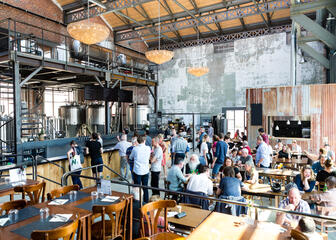 Binnenzicht van restaurant. De bar staat centraal rond de brouwerij. De lange tafels in het midden dienen om bij elkaar aan te schuiven, zoals thuis.
