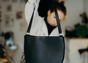 La designer Griet Aesaert tient en l'air un sac à main en forme de croissant terminé et le vérifie à nouveau.