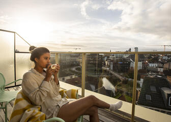 Femme dégustant son café sur la terrasse d'une des suites, vue sur la ville de Gand.