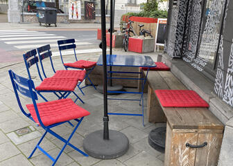Acogedora terraza con sillas azules con cojines rojos, un banco de madera y sombrilla