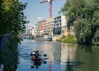 kano met 2 personen op het water met gebouwen op de achtergrond