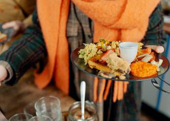 Persoon met oranje sjaal houdt bord met eten vast