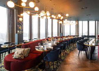 Photo de l’espace restaurant au Skybar avec un grand canapé rouge au milieu, des tables dressées et des sièges bleu foncé 
