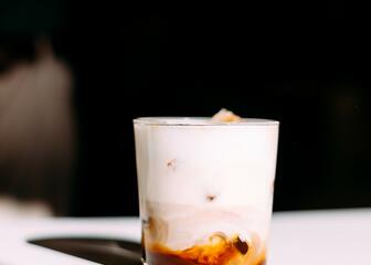 White table with a glass filled with milk and a layer of coffee