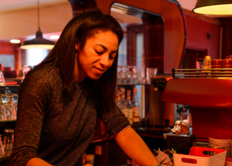 Una mujer sirve leche con un café en el mostrador de la cafetería