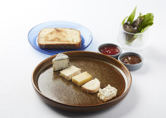 bruin bord met assortiment kazen, blauw bord met snede brood, 2 potjes met chutney