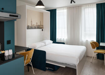 Schlafzimmer mit Klappbett, moderner Küche, Essecke und einem weißen Hängetisch mit dunkelgelbem Stuhl 