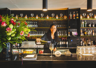 Woman pouring a glass of white wine while smiling behind the bar