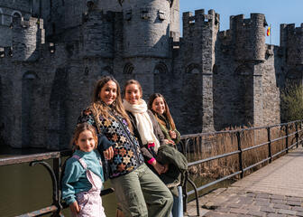 Tiany pose avec ses trois filles devant le château gris des comtes à Gand par une journée ensoleillée