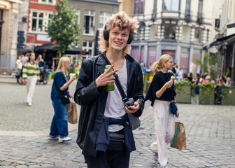 Jonge goedlachse man wandelt met koptelefoon door de straten van Gent