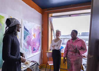 Three artists hold a conversation near some painted canvases.