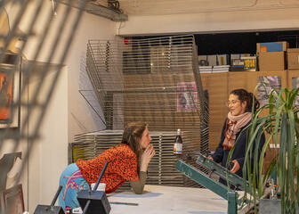 Een bezoeker en een kunstenaar voeren een gesprek in een zeefdrukatelier.