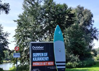 Dobber station met een SUP-board tegen op een groen veld met een vijver op de achtergrond