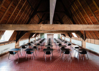 Holzbalken an der Decke mit fünf Reihen von Stühlen an einem Konferenztisch darunter