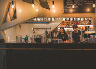 Two people stand in the bar in a alcove set in the white wall