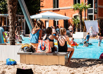 3 mensen zitten op een bankje in het zand