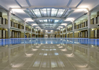 Overzichtsfoto van het zwembad, waar niemand aanwezig is. Het plafond is weerspiegeld in rimpelloos water.