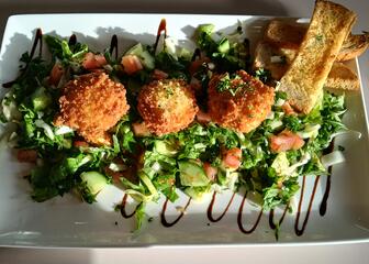 Gericht aus frittierten Bällchen mit Stücken von geröstetem Brot auf einem Bett aus Salat, Tomate und Gurke, mit Balsamico, serviert auf einem weißen Teller
