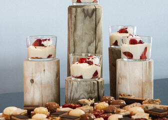 Wooden tray filled with small desserts, such as chocolate mousse, in glass jars.