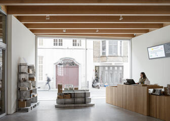 Onthaalmedewerker zit aan het indrukwekkende eiken baliemeubel in de inkomhal van Design Museum Gent.